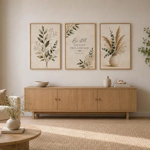 Könnte beinhalten: Ein Set aus drei rechteckigen Wandbildern in hellen Holzrahmen. Das linke Bild zeigt grüne botanische Blätter, das mittlere Bild enthält den Text Be still and know that I am God Psalm 46:10 und das rechte Bild zeigt getrocknetes Pampasgras.