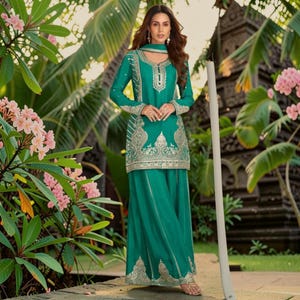 May include: A teal long-sleeved tunic and matching wide-leg trousers set featuring intricate silver embroidery along the neckline, sleeves, and hemline. The garment includes a coordinating scarf draped around the neck with matching silver detailing.