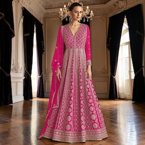 May include: A floor-length fuchsia gown featuring a deep V-neckline, long sleeves, and an intricate silver metallic embroidered pattern throughout the bodice and skirt. A matching fuchsia dupatta with silver embroidery is draped over one shoulder.