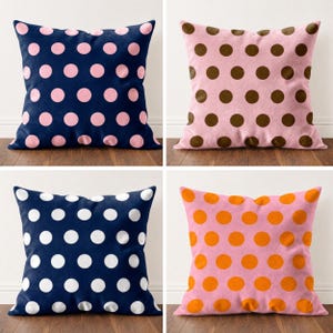 Op de afbeelding: Een set van vier vierkante sierkussens met stippenpatronen. Linksboven marineblauw met lichtroze stippen, rechtsboven lichtroze met bruine stippen, linksonder marineblauw met witte stippen en rechtsonder lichtroze met oranje stippen.