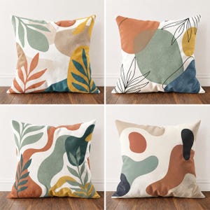 Può includere: Un set di quattro cuscini quadrati con disegni astratti, forme organiche e motivi a foglia. La tavolozza dei colori include tonalità terracotta, verde salvia, giallo senape, blu navy e crema. Ogni cuscino presenta un motivo unico.