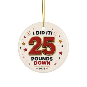 May include: A round white ceramic ornament hanging from a gold string. The text reads I DID IT! 25 POUNDS DOWN 2026. The number 25 is large, red, and gold-bordered. The design includes small red and gold stars and confetti accents around the text.