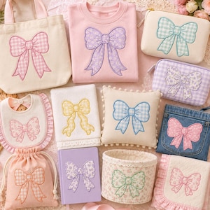 以下が含まれることがあります： 刺繍されたリボンが施されたアイテムのコレクション。クリーム色のトートバッグ、ピンクのスウェットシャツ、クリーム色のファスナー付きポーチ、紫色のファスナー付きポーチ、ベビー用よだれかけ、白いタオル、クリーム色のクッション、デニムバッグ、巾着袋、ノート、バスケット、ブランケットが含まれています。