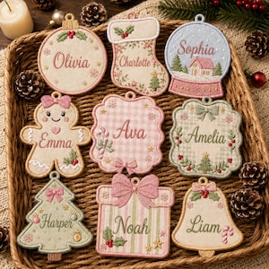 May include: A collection of nine embroidered fabric Christmas ornaments in various shapes including a ball, stocking, snow globe, gingerbread person, square, scalloped rectangle, tree, gift, and bell, each personalised with a name in script.