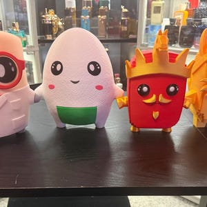 Puede incluir: Cuatro figuras impresas en 3D alineadas. La primera es un personaje blanco con gafas rojas y bata de laboratorio. La segunda es una figura blanca con forma de huevo y vientre verde. La tercera es un rey rojo con corona. La cuarta es un personaje naranja parecido a un gato con gafas.