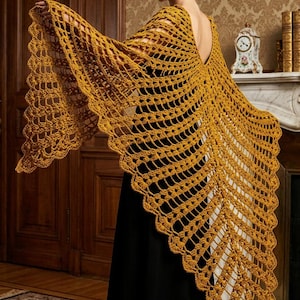 May include: A mustard yellow crochet shawl featuring an intricate openwork pattern with a scalloped edge. The garment is draped over the shoulders, showcasing a V-shaped back design and a detailed, repeating stitch structure throughout the fabric.