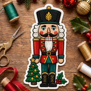 May include: An embroidered nutcracker patch featuring a black hat with a gold emblem, a red and green uniform, and a white beard. The nutcracker stands next to a small green Christmas tree with yellow ornaments and a sprig of holly with red berries.