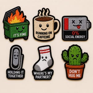 May include: A set of six embroidered patches featuring cartoon designs: a green dumpster on fire with 'IT'S FINE', a coffee mug with 'RUNNING ON CAFFEINE', a battery with '0% SOCIAL ENERGY', a paperclip with 'HOLDING IT TOGETHER', a sock with 'WHERE'S MY PARTNER?', and a cactus with 'DON'T HUG ME'.