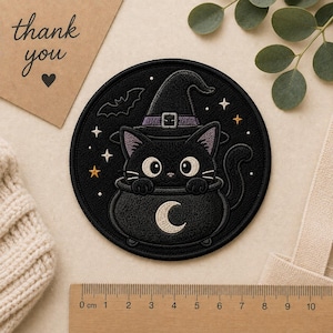 May include: A circular embroidered patch featuring a black cat wearing a purple-banded witch hat, sitting inside a black cauldron with a white crescent moon design. The patch is surrounded by small embroidered stars and a bat, measuring 3.5 inches.