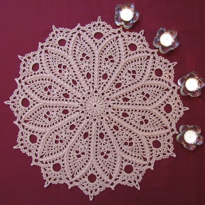 May include: A beige crocheted doily with a delicate floral pattern, surrounded by four small glass candle holders with white candles.
