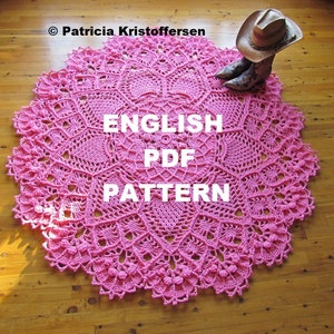 Puede incluir: Un patrón de ganchillo circular rosa, con el texto "ENGLISH PDF PATTERN" en blanco. El patrón presenta intrincados diseños florales y geométricos. Un sombrero de vaquero y botas son visibles en el fondo.