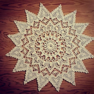 May include: A large, cream-colored crocheted doily with a starburst design. The doily is made of delicate, intricate stitches and has a lacy appearance.