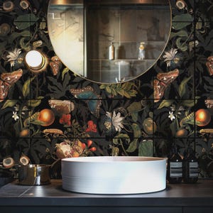 Könnte beinhalten: Ein weißes Aufsatzwaschbecken aus Keramik steht auf einer dunklen Arbeitsplatte vor einer Wand mit schwarzer Tapete, die ein botanisches Muster aus Schmetterlingen, Orangen und weißen Blüten zeigt. Ein runder Spiegel reflektiert den Raum.