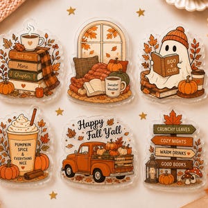 Op de afbeelding: Een set van zes transparante acrylstickers met herfstthema's. De ontwerpen bevatten een stapel boeken met een mok, een raam met een deken, een lezend spookje, een pompoendrankje, een oranje vrachtwagen en een wegwijzer met herfstteksten.