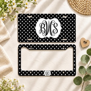 May include: A black license plate and a matching black license plate frame, both featuring a white polka dot pattern. The plate displays a central white scalloped label with the black monogram letters BWS in a decorative script font.