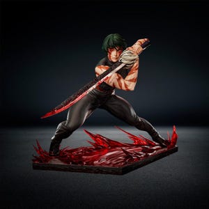 May include: A collectible figurine of a character with short dark green hair, wearing a black outfit with red markings on the skin. The figure holds a long, dark, textured sword and stands on a base featuring a translucent red, jagged, liquid-like effect.