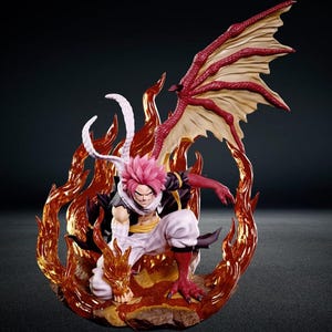 May include: A detailed anime character figurine featuring a figure with pink hair, white pants, and a black vest, crouched in a dynamic pose. The figure has a large red dragon wing, a scaled arm, and is surrounded by translucent orange flame effects.