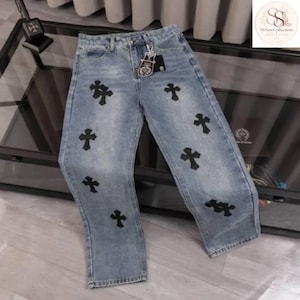 以下が含まれることがあります： ストレートレッグカット、ボタンとジッパーフライ、前面に配置された複数の黒い十字架型のパッチが特徴のライトブルーのデニムジーンズ。ウエストバンドには、小さな銀色の金属製チャームが付いた黒いブランドタグが取り付けられています。