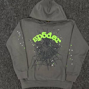 Könnte beinhalten: Ein anthrazitfarbener Kapuzenpullover mit einer großen schwarzen Spinnennetz-Grafik auf der Vorderseite. Der Schriftzug "sp5der" ist in hellem Limettengrün in der Mitte aufgedruckt. Kleine weiße und limettengrüne Sternakzente sind auf Vorderseite und Ärmeln verteilt.