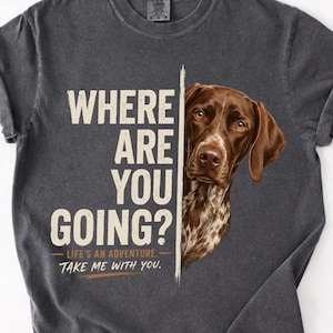 May include: A charcoal grey short-sleeve t-shirt featuring a brown and white German Shorthaired Pointer dog graphic on the right side. The text reads: WHERE ARE YOU GOING? LIFE'S AN ADVENTURE. TAKE ME WITH YOU. The shirt has a crew neckline.