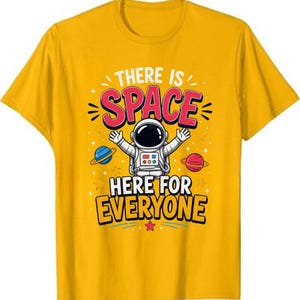 May include: A mustard yellow t-shirt featuring a graphic of an astronaut with arms raised. The text reads THERE IS SPACE HERE FOR EVERYONE. The design includes a blue planet with rings on the left and a red planet with rings on the right, plus stars.
