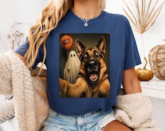 May include: A navy blue short-sleeve t-shirt featuring a graphic print of a German Shepherd dog taking a selfie with a ghost holding an orange balloon with the text BOO printed on it. The shirt has a crew neckline and a relaxed fit design.