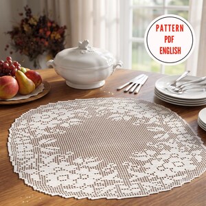 Puede incluir: Un tapete de ganchillo blanco redondo con un patrón floral detallado y un borde festoneado. Un gráfico circular en la esquina superior derecha contiene el texto rojo PATTERN PDF ENGLISH. El tapete se muestra sobre una mesa de madera.