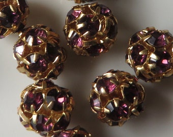 May include: A collection of spherical beads featuring a gold-toned metal cage structure embedded with deep purple faceted stones. Each bead has a rounded, openwork design that secures the dark violet crystals within the metallic framework.