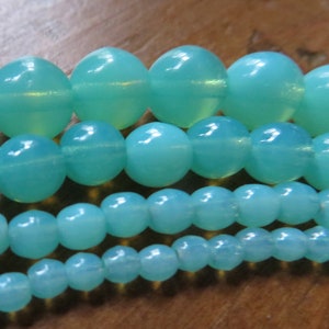 May include: A set of turquoise blue gemstone beads in various sizes. The beads are round and smooth, and they are arranged in rows of decreasing size.