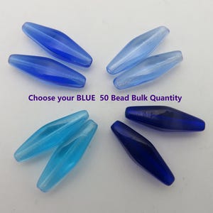 May include: An assortment of blue glass beads in various shades, from light to dark, arranged on a white surface. The beads are elongated and oval-shaped. Text on the image reads "Choose your BLUE 50 Bead Bulk Quantity."