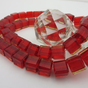 May include: A strand of red glass beads, each bead is a square with a slightly frosted finish.