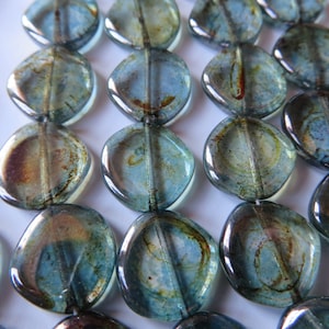 May include: Close-up of a collection of blue and brown glass beads. The beads are oval-shaped with a hole running through the center. The beads have a marbled appearance with a mix of blue and brown tones.