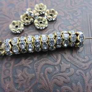 May include: A strand of clear crystal beads with gold settings. The beads are arranged in a spiral pattern. There are also several loose beads in the image.