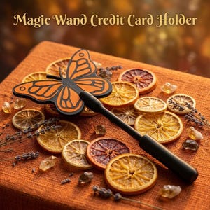 May include: A Magic Wand Credit Card Holder featuring a black and orange butterfly-shaped top attached to a long, slender black handle. The design includes intricate black wing patterns on an orange background, presented as a functional accessory.