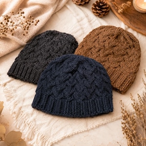 May include: Three knit beanies in dark gray, navy blue, and brown. Each beanie features a textured cable knit pattern throughout the main body and a ribbed knit cuff at the base. The hats are arranged in a cluster, showcasing the distinct colors.