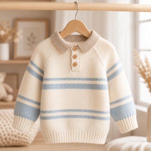 May include: A cream-colored long-sleeve knit sweater featuring a light blue horizontal striped pattern, a ribbed collar in a darker beige tone, and a three-button placket with small wooden buttons. The garment has raglan sleeves and ribbed cuffs.