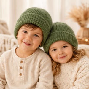 May include: Two matching olive green ribbed knit beanies with folded cuffs. The beanies are made of a soft, textured yarn and feature a classic pull-on style that covers the ears, providing a simple and functional head covering for cold weather.