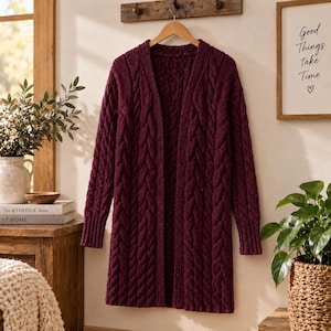 May include: A long-sleeved, open-front cardigan in a deep burgundy color. The garment features a prominent vertical cable knit pattern throughout the body and sleeves, with ribbed cuffs and a ribbed collar edge, hanging from a wooden hanger.