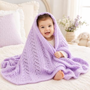 Könnte beinhalten: Eine weiche, hellviolette gestrickte Babydecke mit einem zarten Zickzack- und Spitzenmuster. Die Decke ist über ein lächelndes Kleinkind drapiert und zeigt die komplizierte Textur des Garns sowie das durchbrochene Design im gesamten Stoff.