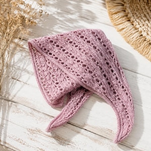 Pode incluir: Um xale triangular de tricô na cor rosa seco, apresentando um intrincado padrão de renda aberta com detalhes de ilhós repetitivos. O tecido tem uma aparência macia e texturizada com um formato pontiagudo e bordas acabadas, exibindo um tricô delicado.