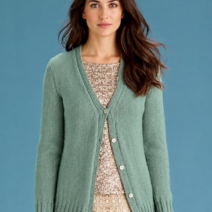 May include: A sage green knit cardigan featuring a V-neckline, long sleeves, and a front button closure with five light-coloured buttons. The cardigan has a ribbed hem and cuffs, worn over a gold sequined top and a beige lace skirt.