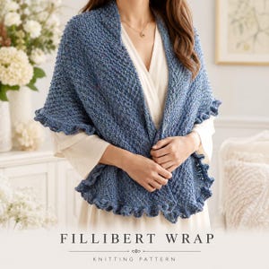 Może przedstawiać: Niebieska dzianinowa chusta o fakturowanym splocie z falbanką na krawędzi. Odzież jest narzucona na białą bluzkę. Tekst FILLIBERT WRAP KNITTING PATTERN znajduje się na dole obrazu i jest zapisany wyraźną, ciemną czcionką szeryfową.