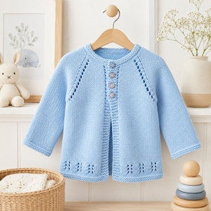 May include: A light blue long-sleeve knit cardigan featuring a round neckline, four small floral-patterned buttons down the center, and decorative eyelet detailing along the raglan sleeves and the bottom hem of the garment.