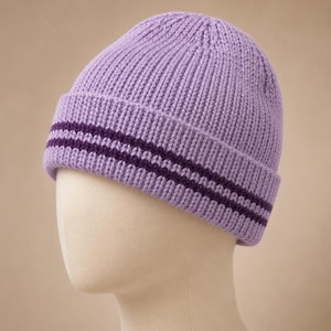 May include: A light purple knitted beanie hat featuring a folded cuff with two horizontal dark purple stripes. The hat is constructed with a vertical ribbed texture throughout, providing a consistent pattern from the crown down to the bottom edge.