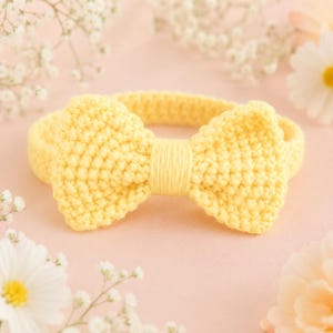 May include: A bright yellow crochet headband featuring a prominent, textured bow at the center. The bow is constructed with a dense, uniform stitch pattern and is cinched in the middle with smooth, vertical yarn wrapping, creating a distinct shape.