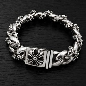 Puede incluir: Una pulsera de eslabones de plata con eslabones redondeados y pulidos, intercalados con elementos decorativos en forma de cruz. La pulsera incluye un cierre de caja rectangular adornado con un emblema central de cruz floral detallada.