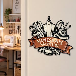 Könnte beinhalten: Ein schwarzes und kupferfarbenes Wandschild mit Näh-Motiven wie einer Schneiderpuppe, Schere, Maßband und Garn mit Nadeln. Ein zentrales kupferfarbenes Banner zeigt den weißen Schriftzug VANESSA'S NÄHSTUBE über einem Nadelkissen.