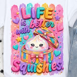 May include: A white t-shirt featuring a colorful graphic of a smiling dumpling inside a striped gift box. The text reads "LIFE is better with Squishies." The design includes pastel-colored brushstrokes, hearts, stars, and a pink bow.