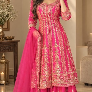 Könnte beinhalten: Eine leuchtend fuchsiafarbene Tunika mit langen Ärmeln und eine passende weite Hose mit aufwendigen Goldstickereien und Spiegelarbeiten. Das Set enthält einen transparenten fuchsiafarbenen Dupatta mit Goldstickerei und Goldohrringe.