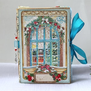May include: A rectangular journal featuring a cover illustration of a blue window frame decorated with Christmas greenery, red roses, and a white bow. A bright teal ribbon is tied to the side, and a silver charm with red and blue beads hangs from the spine.